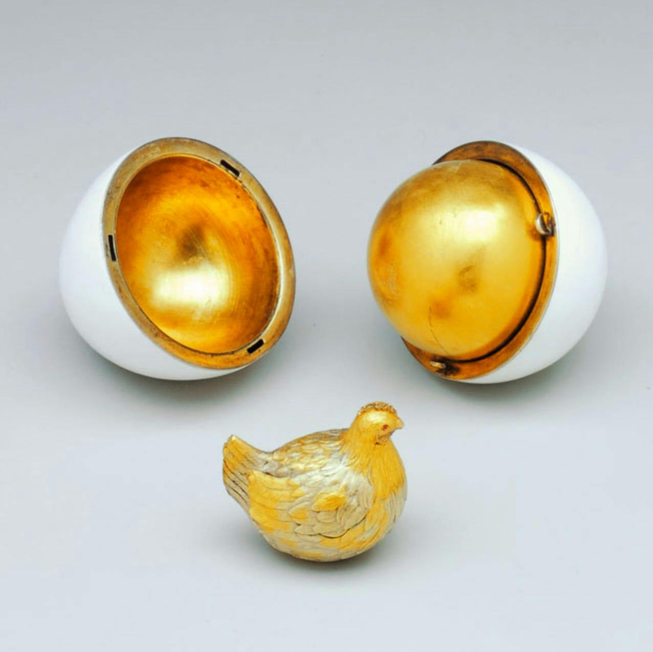 First Hen by Peter Carl Fabergé, 1885. [An egg split apart with a golden inside and a small golden hen in front of it.]