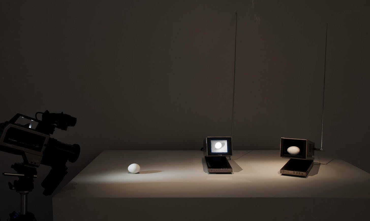 Three Eggs by Nam June Paik, 1975–1982. [An egg on a table is filmed by a camera. Two small monitors beside the egg display its projection.]